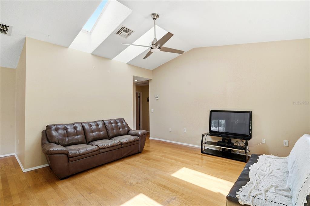 A living room features a brown leather sofa, hardwood floors, and two large skylights — 8160 STURBRIDGE COURT UNIT 8160, WEEKI WACHEE, FL