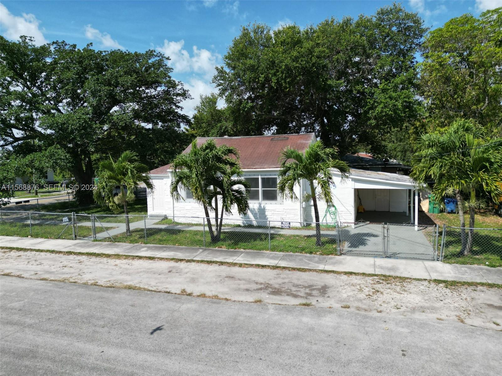 A white one-story house with a brown roof and a carport sits behind a chain-link fence — 2255 NW 63rd St, Miami FL 33147, MIAMI, FL