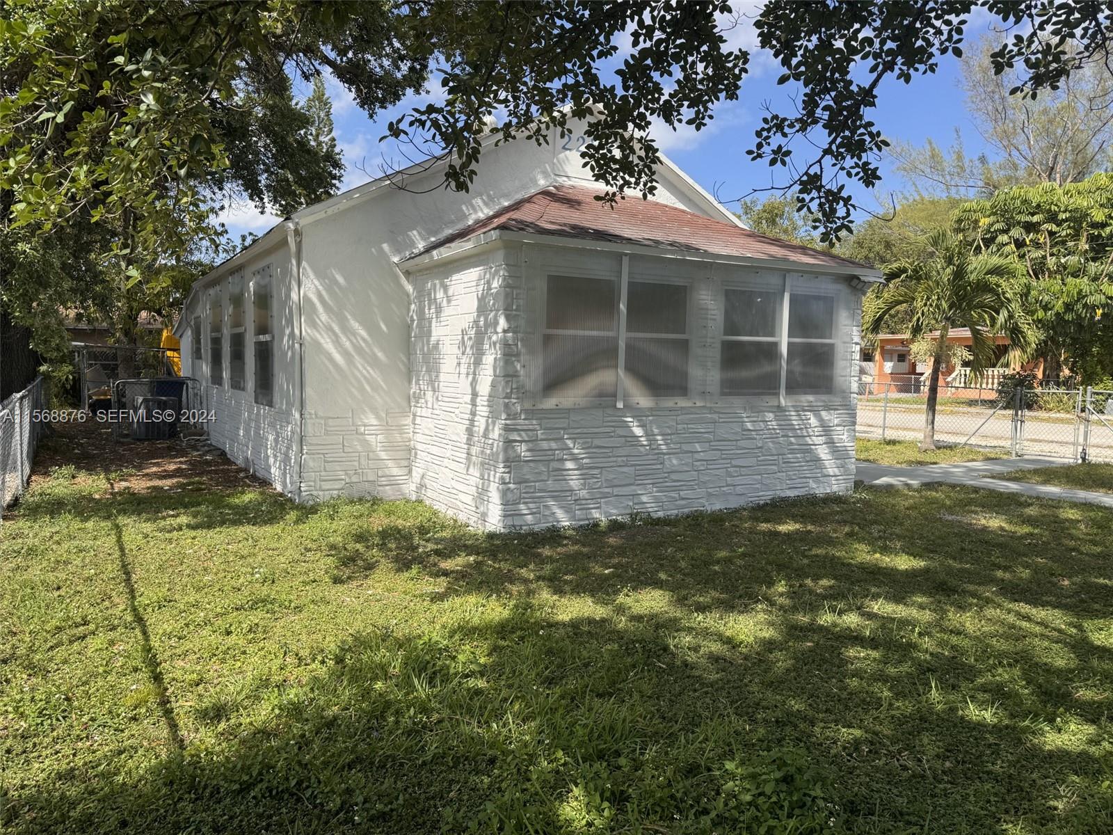 A white house with a stone-textured base and a screened-in porch sits on a lawn — 2255 NW 63rd St, Miami FL 33147, MIAMI, FL