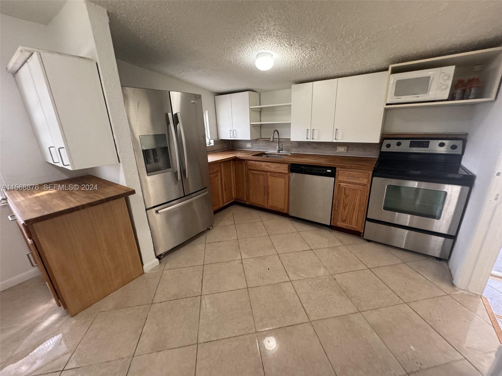 A kitchen features stainless steel appliances, white upper cabinets, wood lower cabinets, and tile flooring — 2255 NW 63rd St, Miami FL 33147, MIAMI, FL