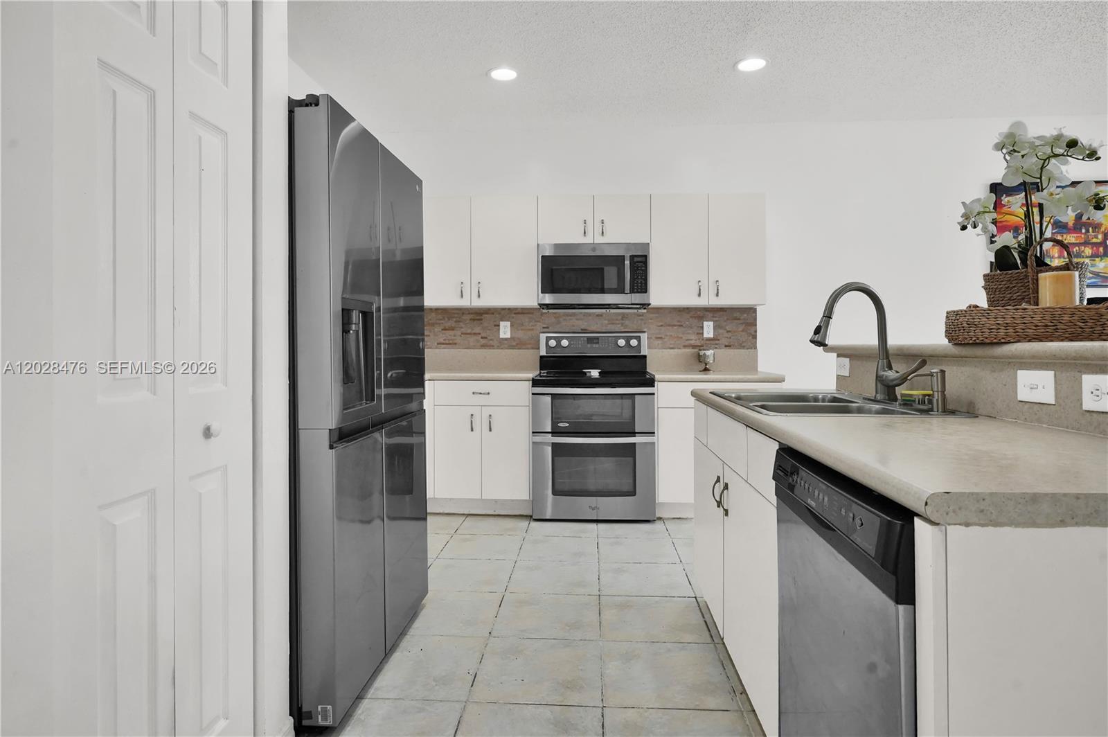 A kitchen features white cabinets, stainless steel appliances, a tiled floor, and a breakfast bar — HOMESTEAD, FL