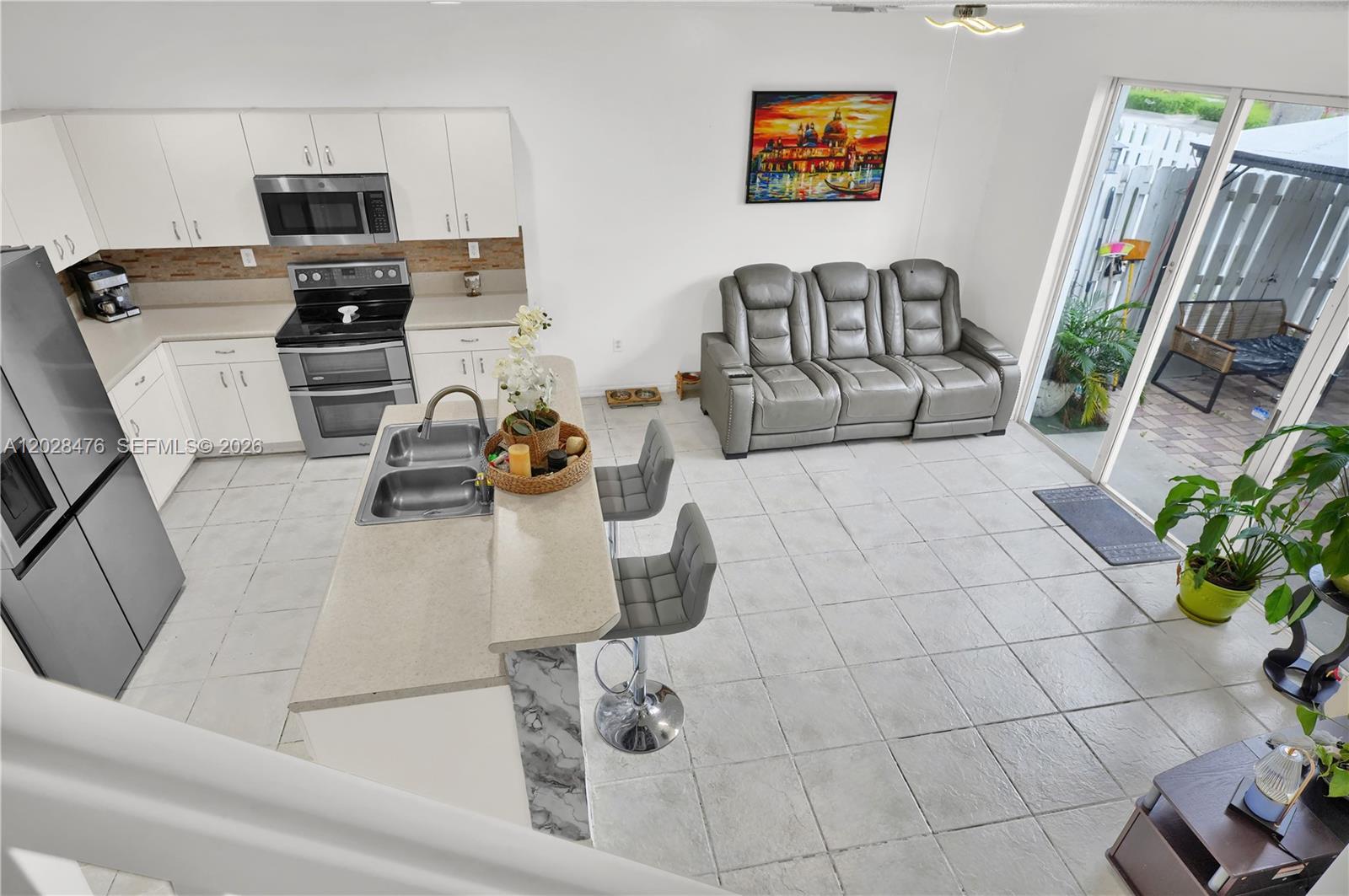 An open-concept kitchen and living area features white cabinetry, a breakfast bar, and gray furniture — HOMESTEAD, FL