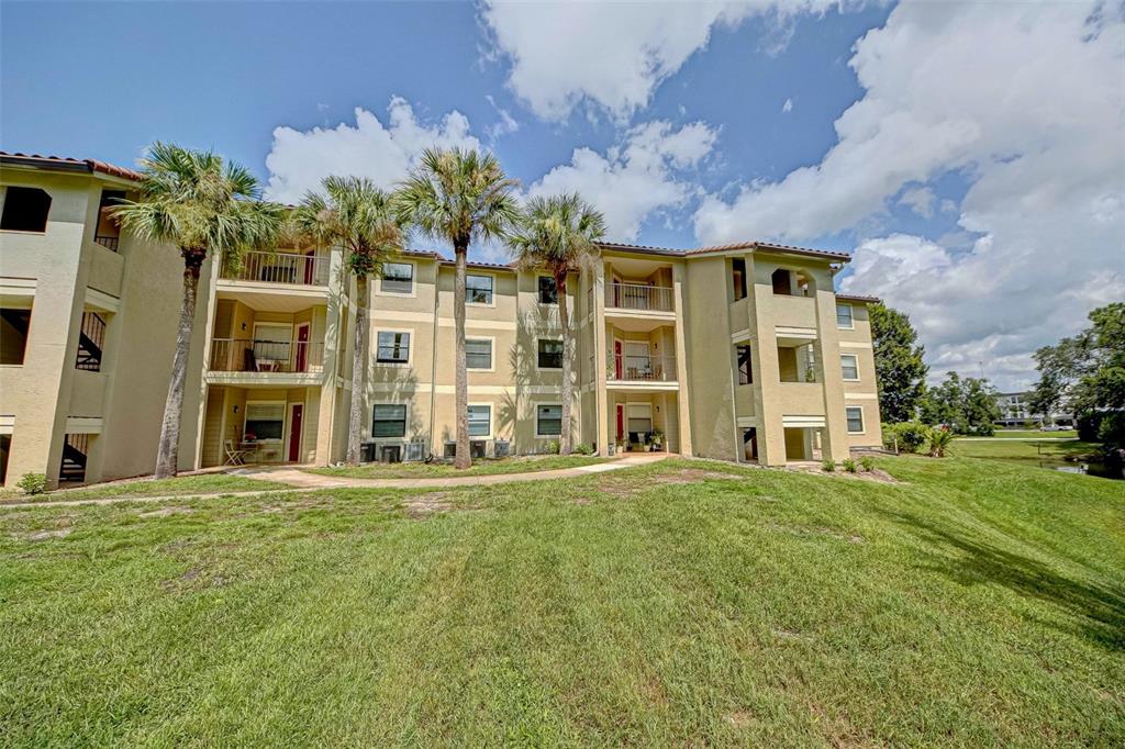 A three-story apartment building with tan stucco walls, balconies, and palm trees on a lawn — 3038 PARKWAY BOULEVARD UNIT 305, KISSIMMEE, FL