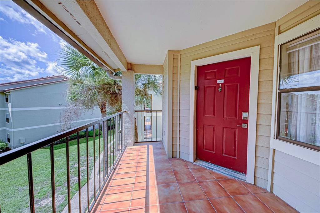 A red front door opens onto a tiled balcony with a metal railing overlooking grass — 3038 PARKWAY BOULEVARD UNIT 305, KISSIMMEE, FL