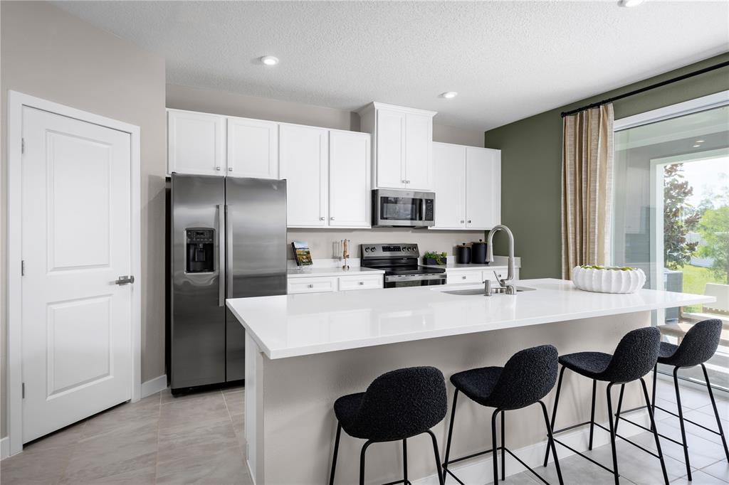 A modern kitchen features white cabinetry, stainless steel appliances, a quartz island, and bar seating — 3964 ADDIE WAY, MELBOURNE, FL