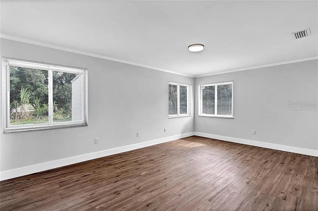 An empty room features light gray walls, wood-look flooring, and three windows — 4289 YUCATAN CIRCLE, PORT CHARLOTTE, FL