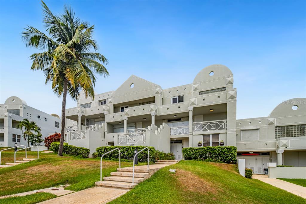 A multi-story, light-colored residential building features balconies, geometric architectural details, and a palm tree — N St. COND. COSTA DORADA II UNIT L208, DORADO, PR