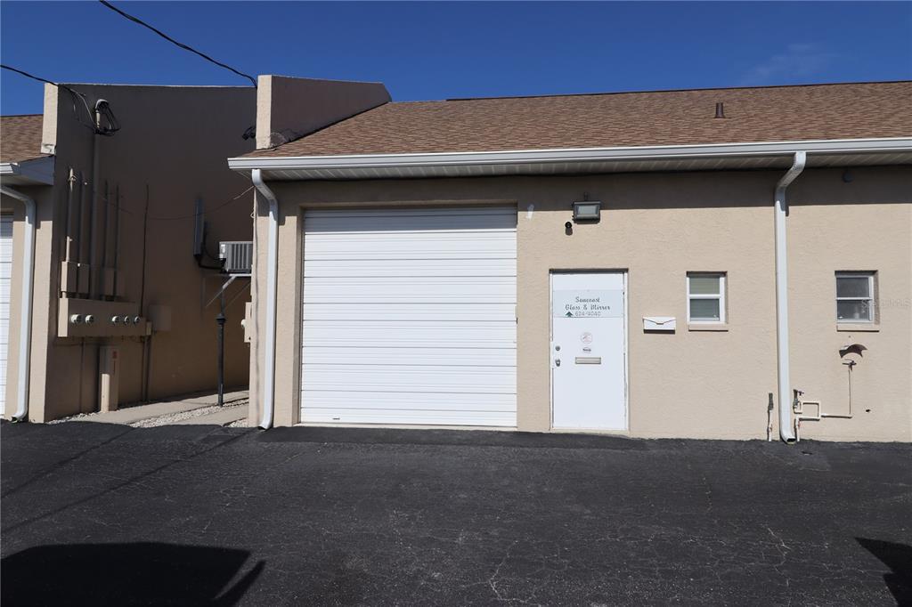 A commercial building exterior features a white roll-up garage door and a single entry door — 18350 PAULSON DRIVE UNIT D-1, PORT CHARLOTTE, FL