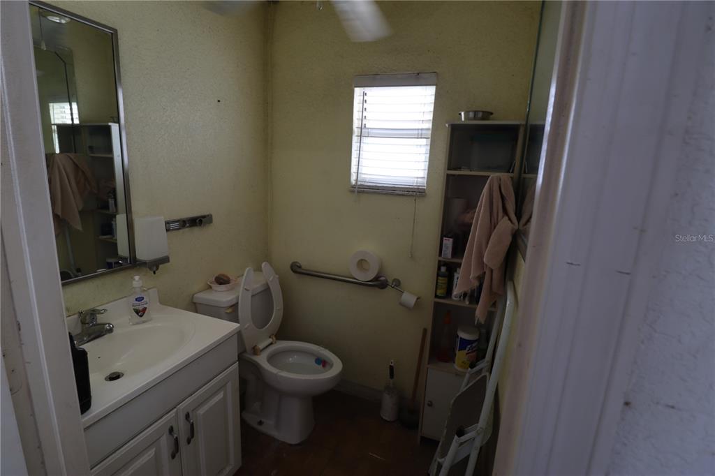A small bathroom features a white vanity, a toilet with a grab bar, and shelving — 18350 PAULSON DRIVE UNIT D-1, PORT CHARLOTTE, FL