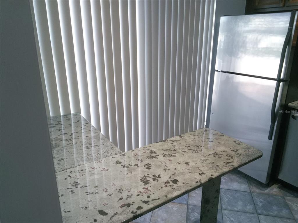A granite countertop breakfast bar sits next to a refrigerator and vertical window blinds — 4209 FOGCUTTER COURT UNIT 4209, TAMPA, FL