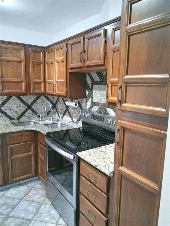 A kitchen features wood cabinets, granite countertops, a stainless steel stove, and patterned tile backsplash — 4209 FOGCUTTER COURT UNIT 4209, TAMPA, FL