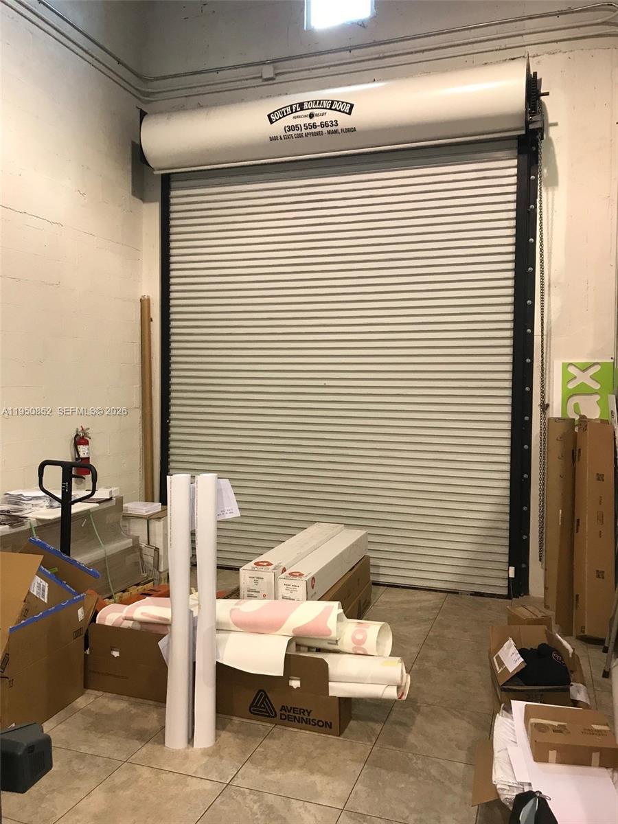 A storage room features a large metal rolling door and tiled flooring — 12300 SW 130th St # 7, Miami FL 33186, MIAMI, FL