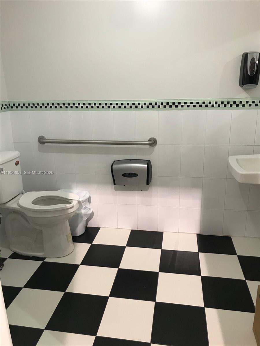 A bathroom features a white toilet, grab bar, paper towel dispenser, and black-and-white checkered flooring — 12300 SW 130th St # 7, Miami FL 33186, MIAMI, FL