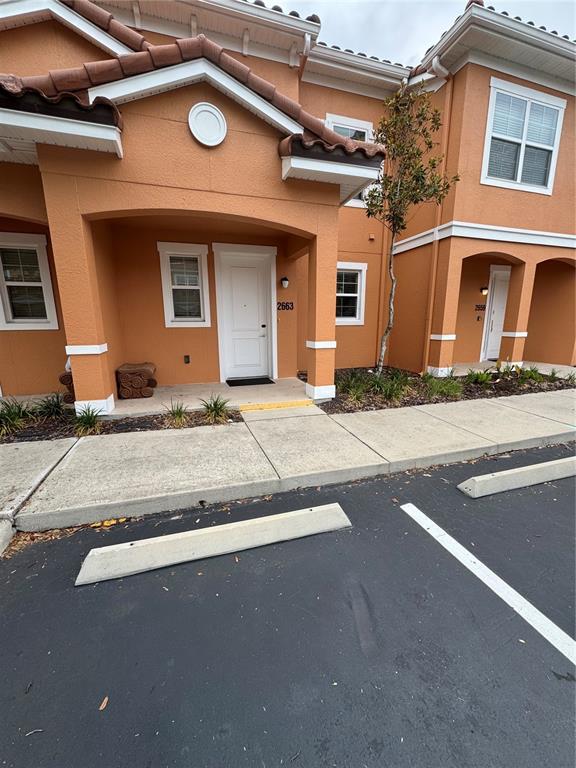 An exterior view of a two-story orange stucco townhouse with a white front door — 2663 ROADSTER LANE, KISSIMMEE, FL