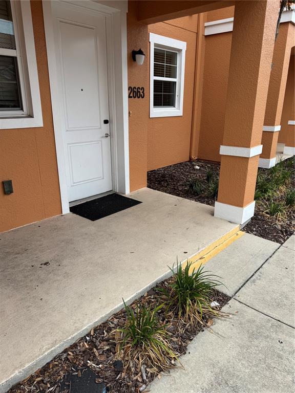 The exterior of a residential building features an orange stucco wall, a white door, and a concrete porch — 2663 ROADSTER LANE, KISSIMMEE, FL