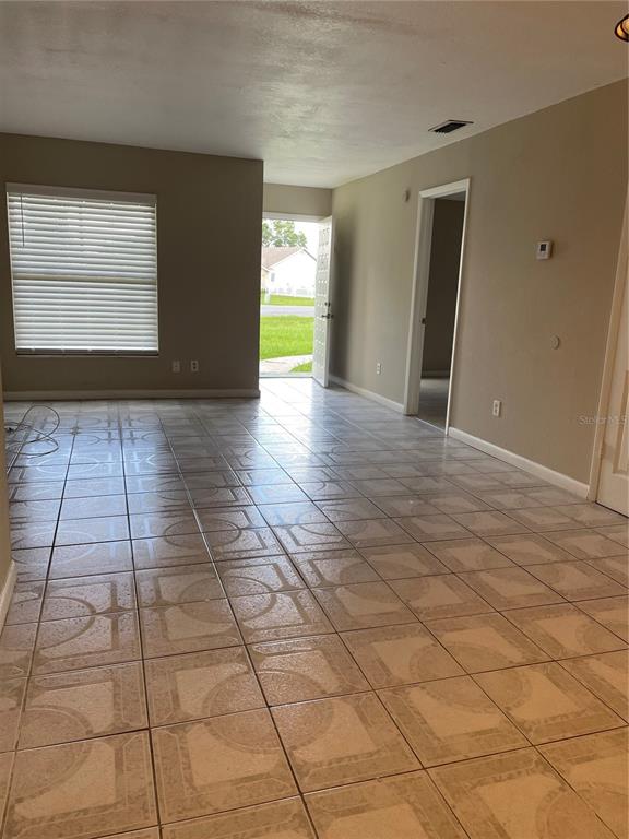 An empty room with beige tile flooring, a window with blinds, and an open doorway — 602 MCKINLEY COURT, KISSIMMEE, FL