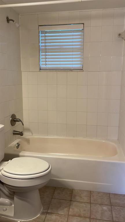 A bathroom features a white toilet, a bathtub with a shower head, and tiled walls — 602 MCKINLEY COURT, KISSIMMEE, FL