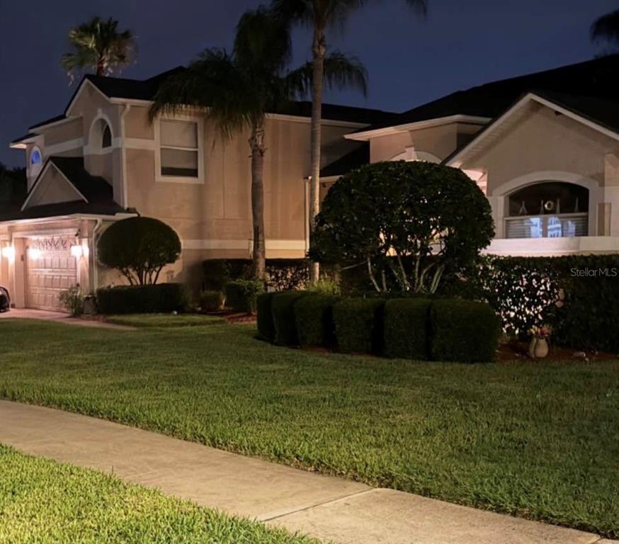 A two-story house exterior at night with a manicured lawn, palm trees, and landscaping — 4552 LAKE CALABAY DRIVE, ORLANDO, FL