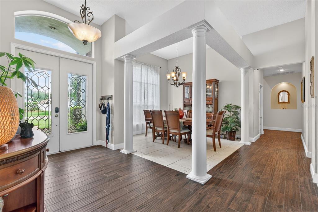 An entryway with wood-look tile floors leads to a dining area defined by white columns — 4552 LAKE CALABAY DRIVE, ORLANDO, FL