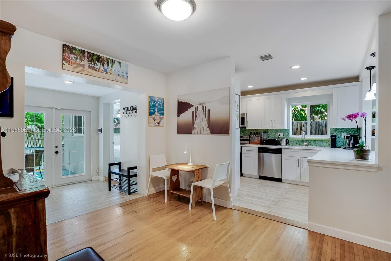 A dining area with hardwood floors connects to a white kitchen and a glass-paned door — 113 SW 2nd St, Hallandale Beach FL 33009, HALLANDALE BEACH, FL