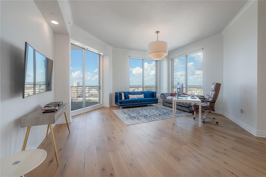 A bright living room features hardwood floors, floor-to-ceiling windows, a blue sofa, and a desk — 449 S 12TH STREET UNIT 2701, TAMPA, FL