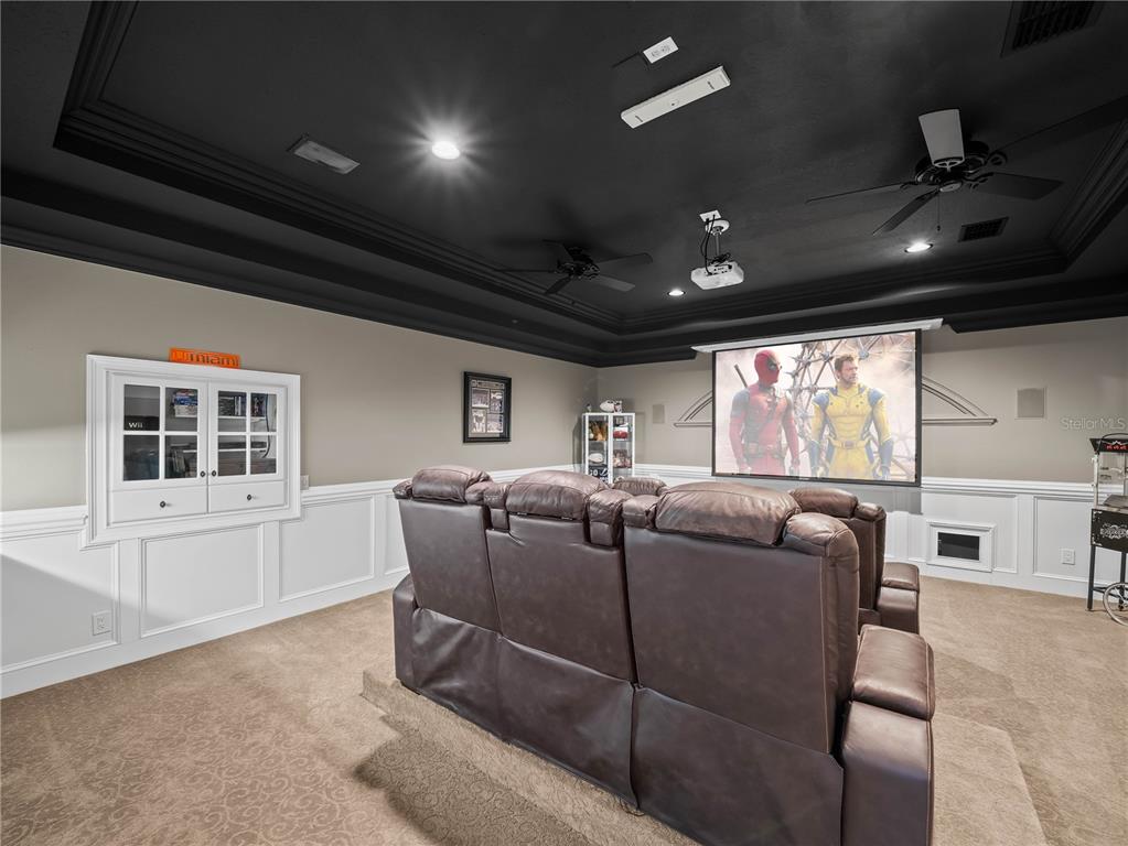 A home theater room features tiered brown leather seating, a projector screen, and black ceilings — 6556 CRESCENT LAKE DRIVE, LAKELAND, FL