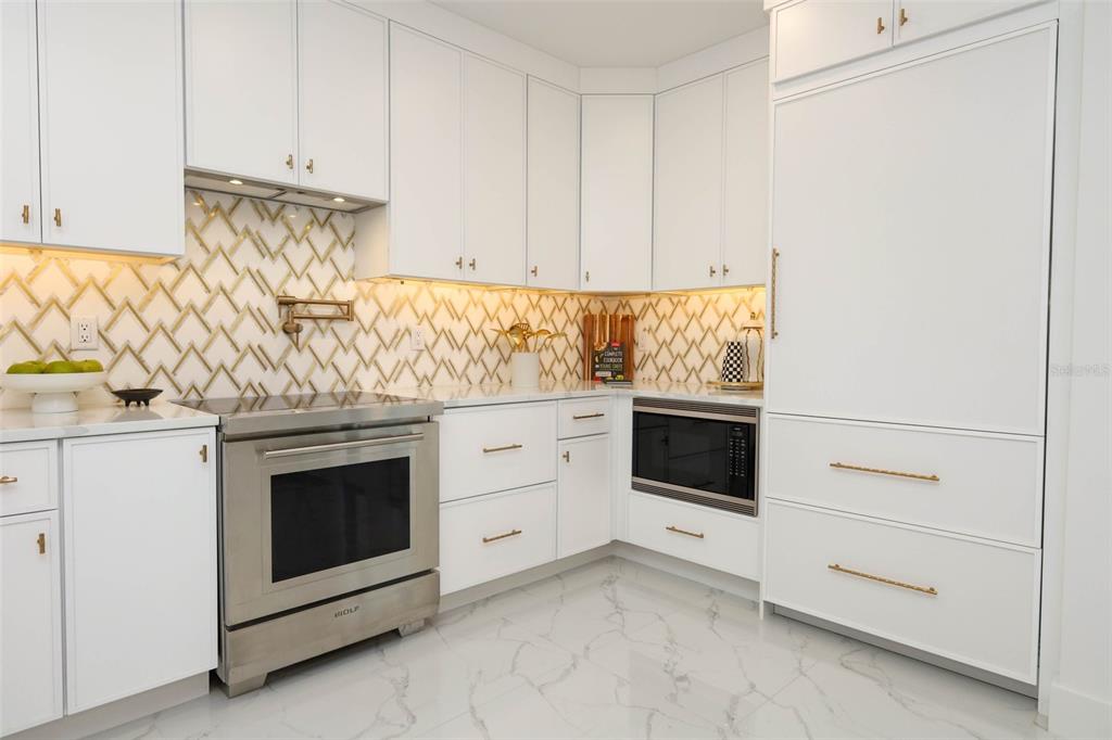 A modern white kitchen features gold hardware, a patterned backsplash, and stainless steel appliances — 2360 OCEAN SHORE BOULEVARD UNIT 29, ORMOND BEACH, FL