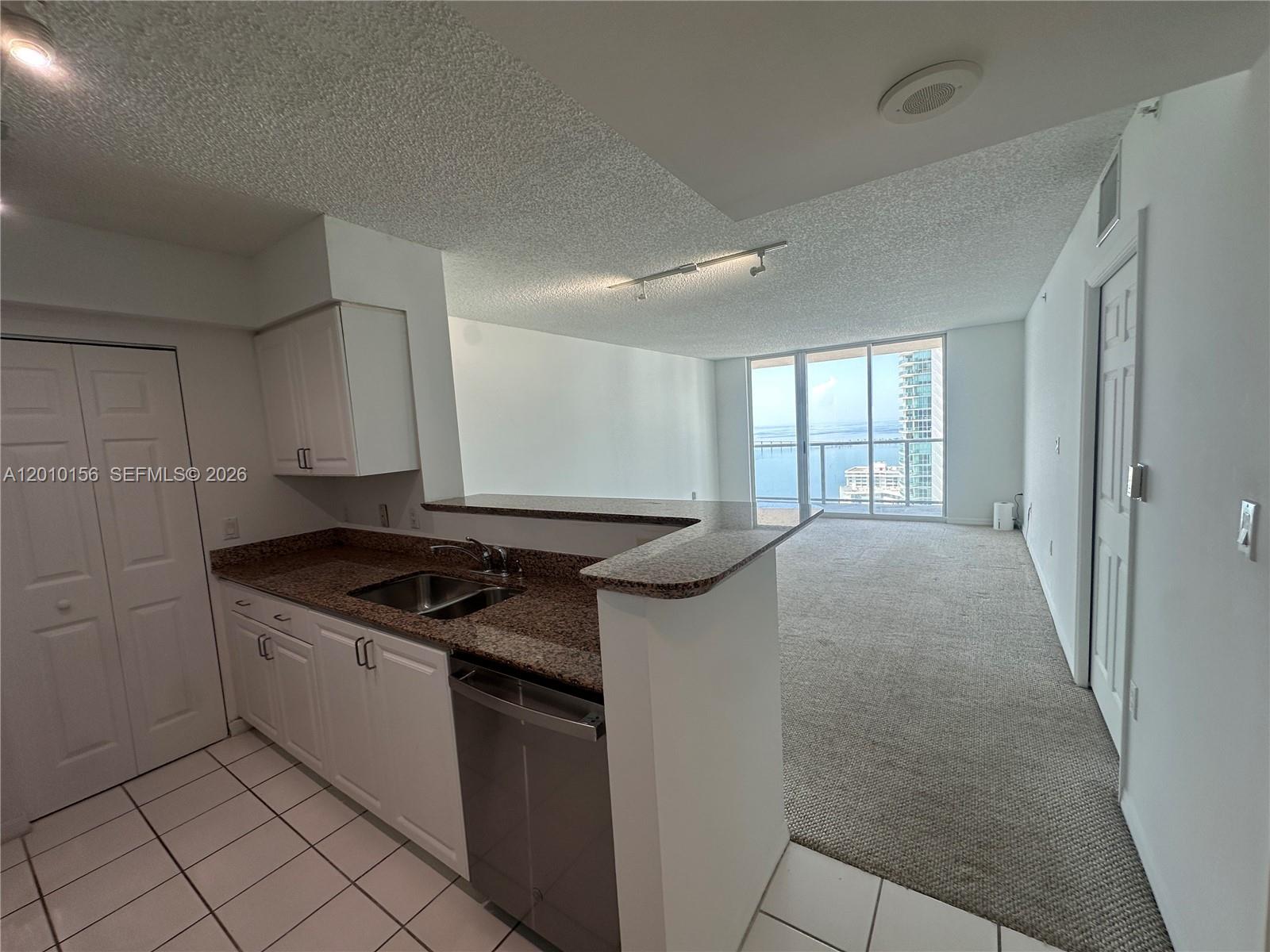 A kitchen with white cabinets and granite countertops overlooks a carpeted living area with balcony — 1155 Brickell Bay Dr # 3007, Miami FL 33131, MIAMI, FL