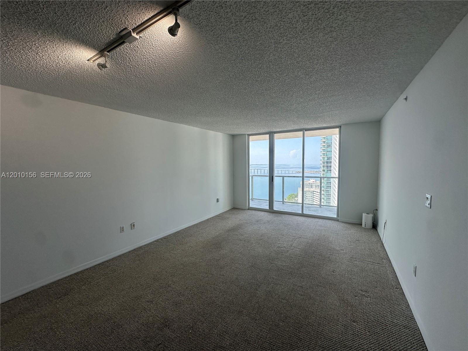 An empty room with beige carpet, white walls, a popcorn ceiling, and a balcony view — 1155 Brickell Bay Dr # 3007, Miami FL 33131, MIAMI, FL