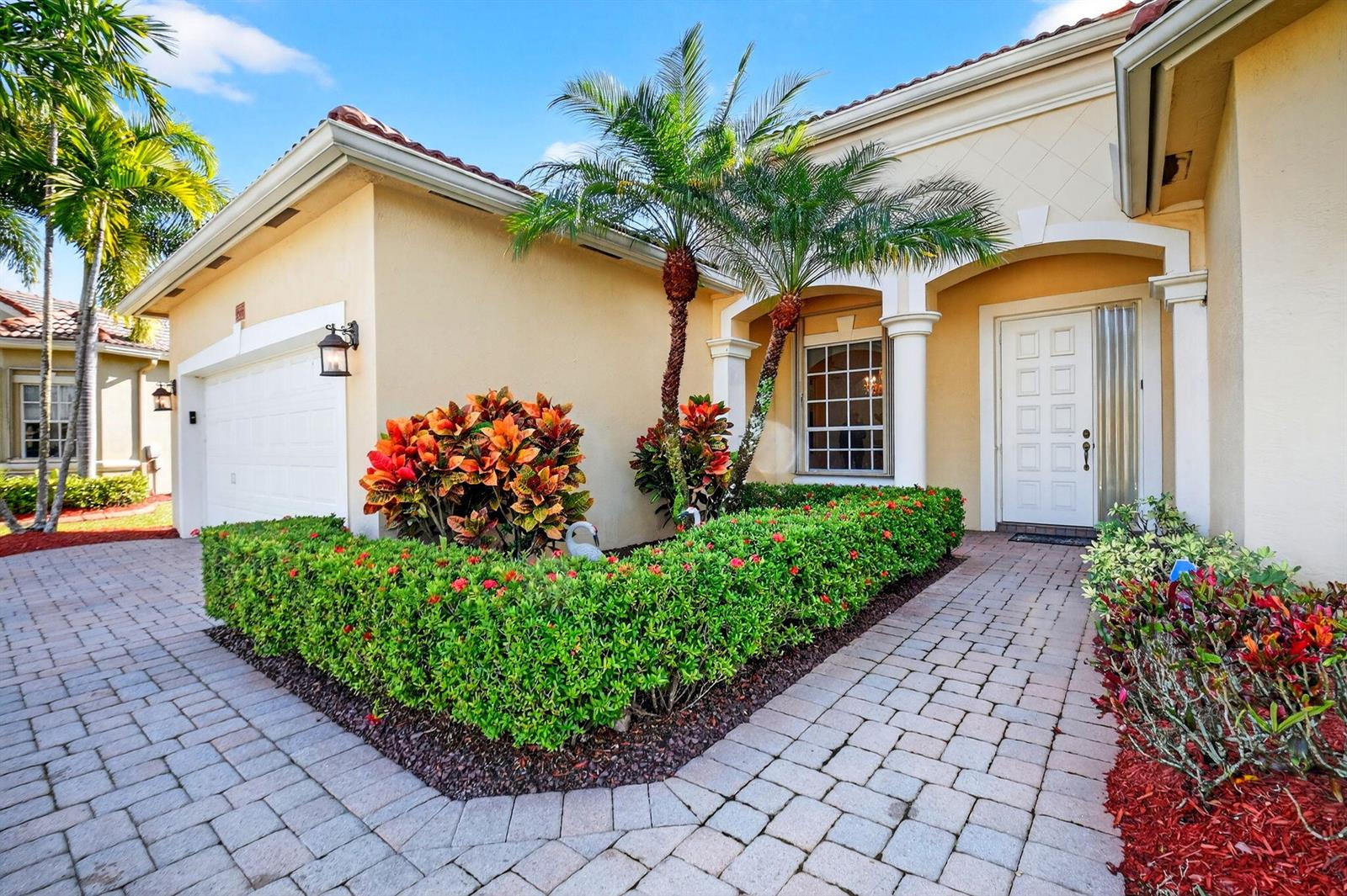 A beige house exterior features a paved walkway, a manicured hedge, and two palm trees — 9566 Lantern Bay Circle, West Palm Beach FL 33411, WEST PALM BEACH, FL