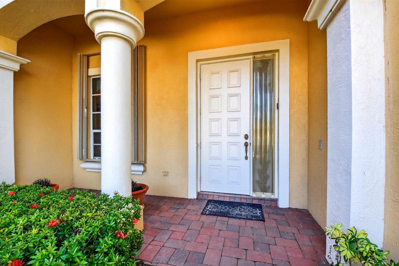 A white front door with a side window sits on a brick porch with columns — 9566 Lantern Bay Circle, West Palm Beach FL 33411, WEST PALM BEACH, FL