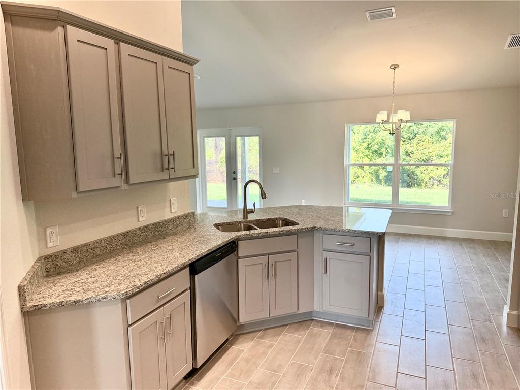 A kitchen features gray cabinets, granite countertops, a stainless steel dishwasher, and tile flooring — 9227 NEWNAN CIRCLE, PORT CHARLOTTE, FL