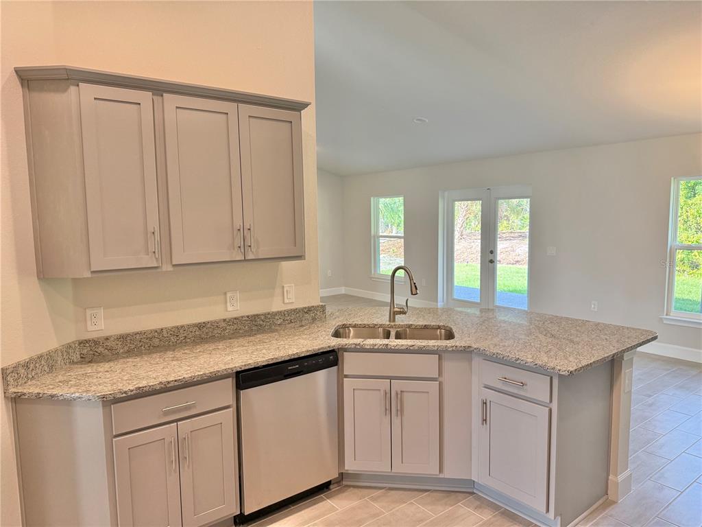 A kitchen features light gray cabinets, granite countertops, a stainless steel dishwasher, and a sink — 9227 NEWNAN CIRCLE, PORT CHARLOTTE, FL