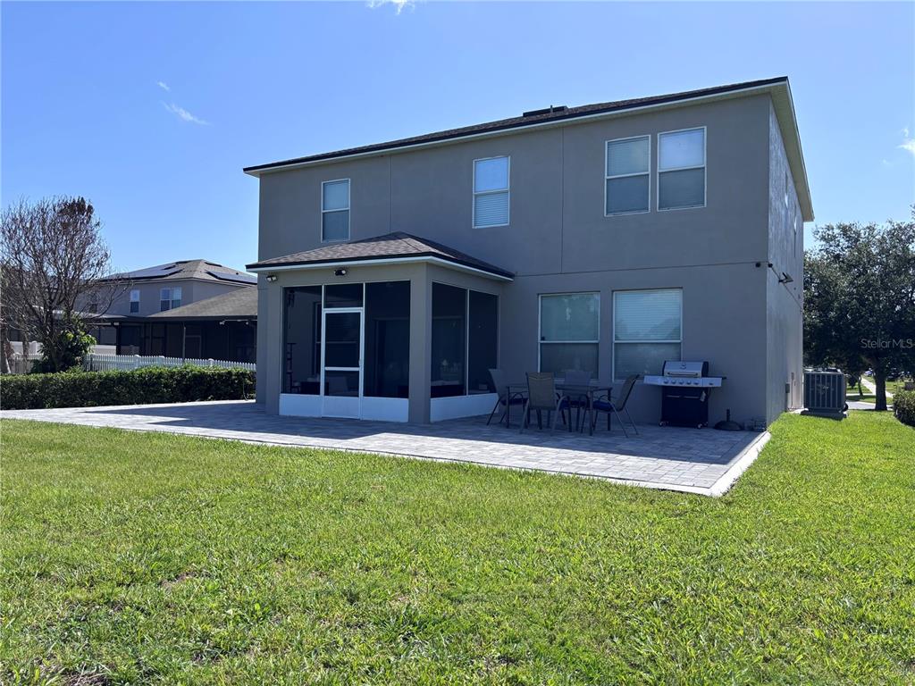 The rear exterior of a two-story house features a screened-in patio and a paved patio area — 2707 RANDAL WAY, KISSIMMEE, FL