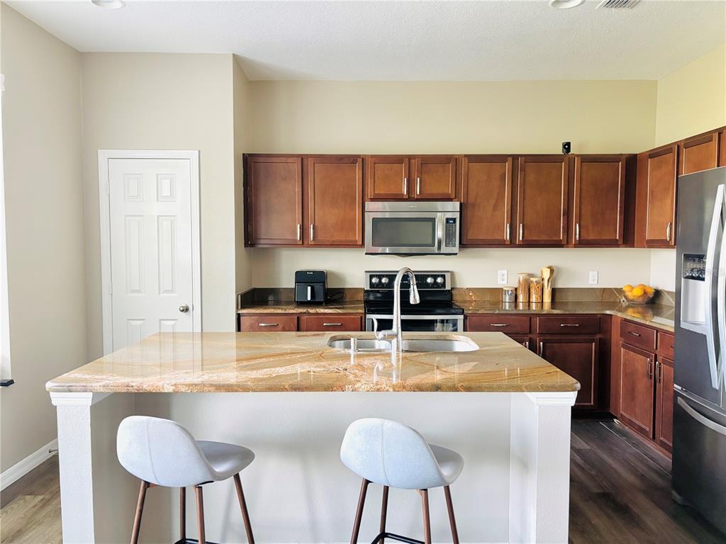 A kitchen features a granite-topped island, wooden cabinetry, stainless steel appliances, and two bar stools — 2707 RANDAL WAY, KISSIMMEE, FL