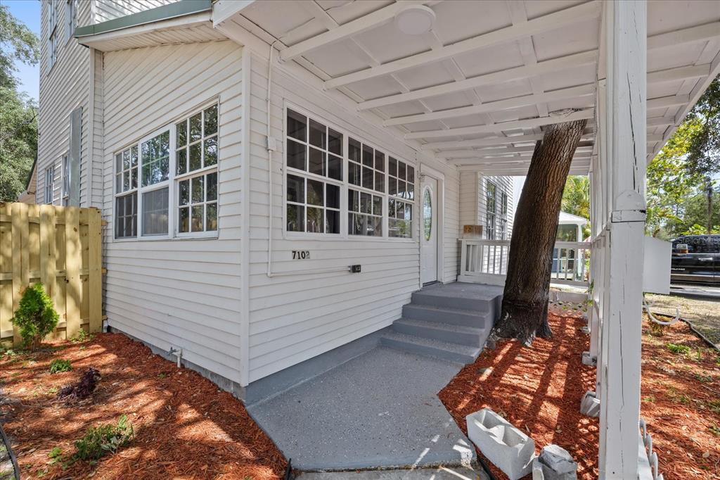 A white house exterior features a covered porch with a tree growing through the roof — 7102 S FITZGERALD STREET, TAMPA, FL