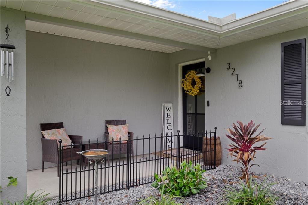 A covered front porch features two wicker chairs, a metal fence, and a front door — 3218 S ROSE AVENUE, INVERNESS, FL
