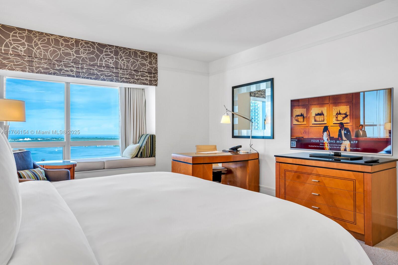 A hotel bedroom features a large bed, a wooden desk, and a window with water views — 1435 Brickell Ave # 3607, Miami FL 33131, MIAMI, FL
