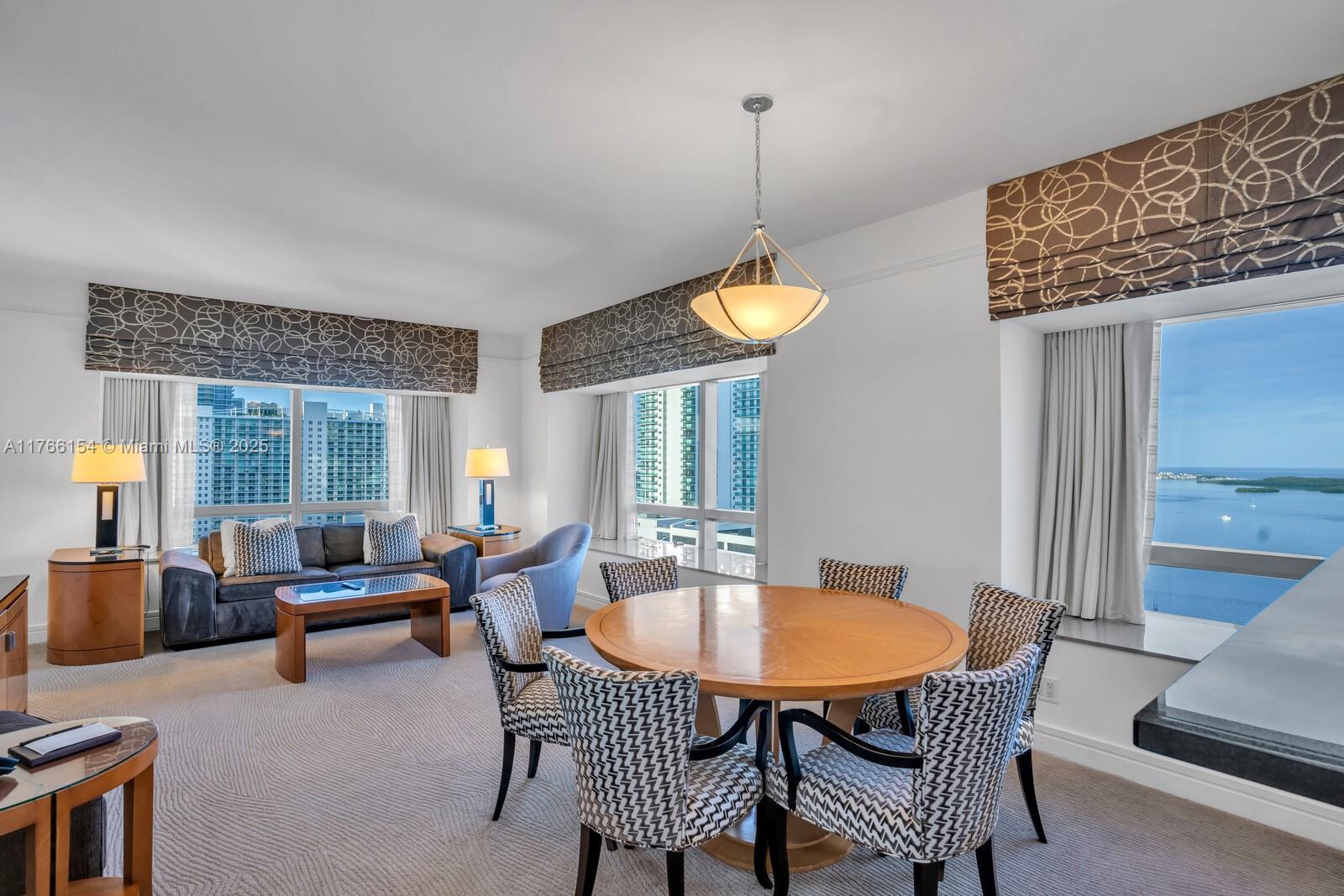 A living and dining area features a round wooden table, patterned chairs, and floor-to-ceiling windows — 1435 Brickell Ave # 3607, Miami FL 33131, MIAMI, FL