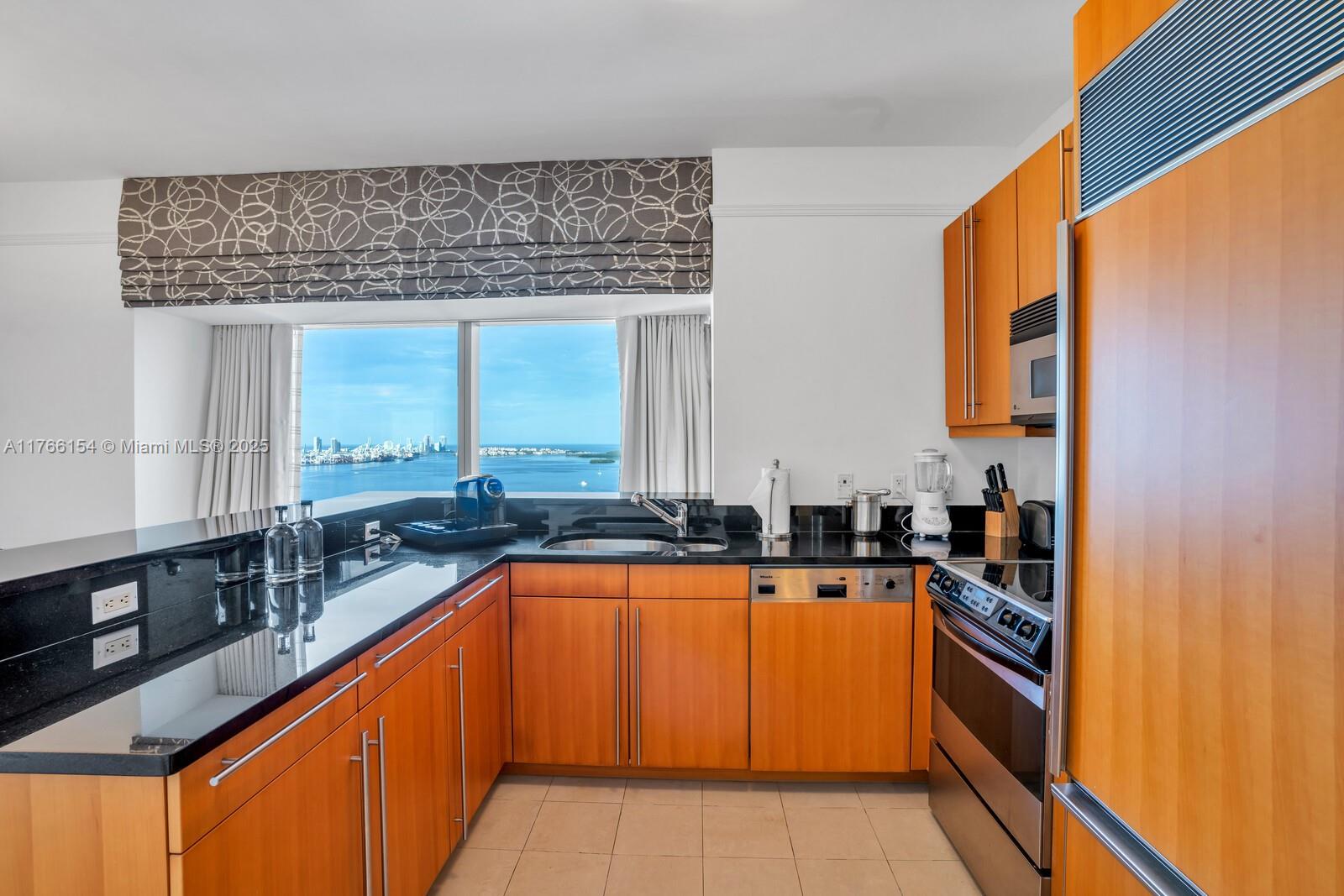 A kitchen features wood cabinets, black countertops, stainless steel appliances, and a water view — 1435 Brickell Ave # 3607, Miami FL 33131, MIAMI, FL