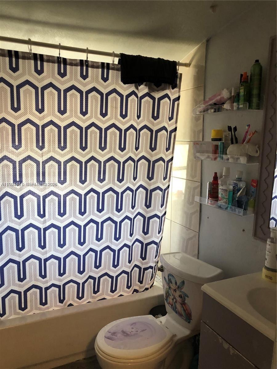 A bathroom features a patterned shower curtain, a toilet with decals, and wall-mounted storage shelves — 2231 SW 57th Ct, Miami FL 33155, MIAMI, FL