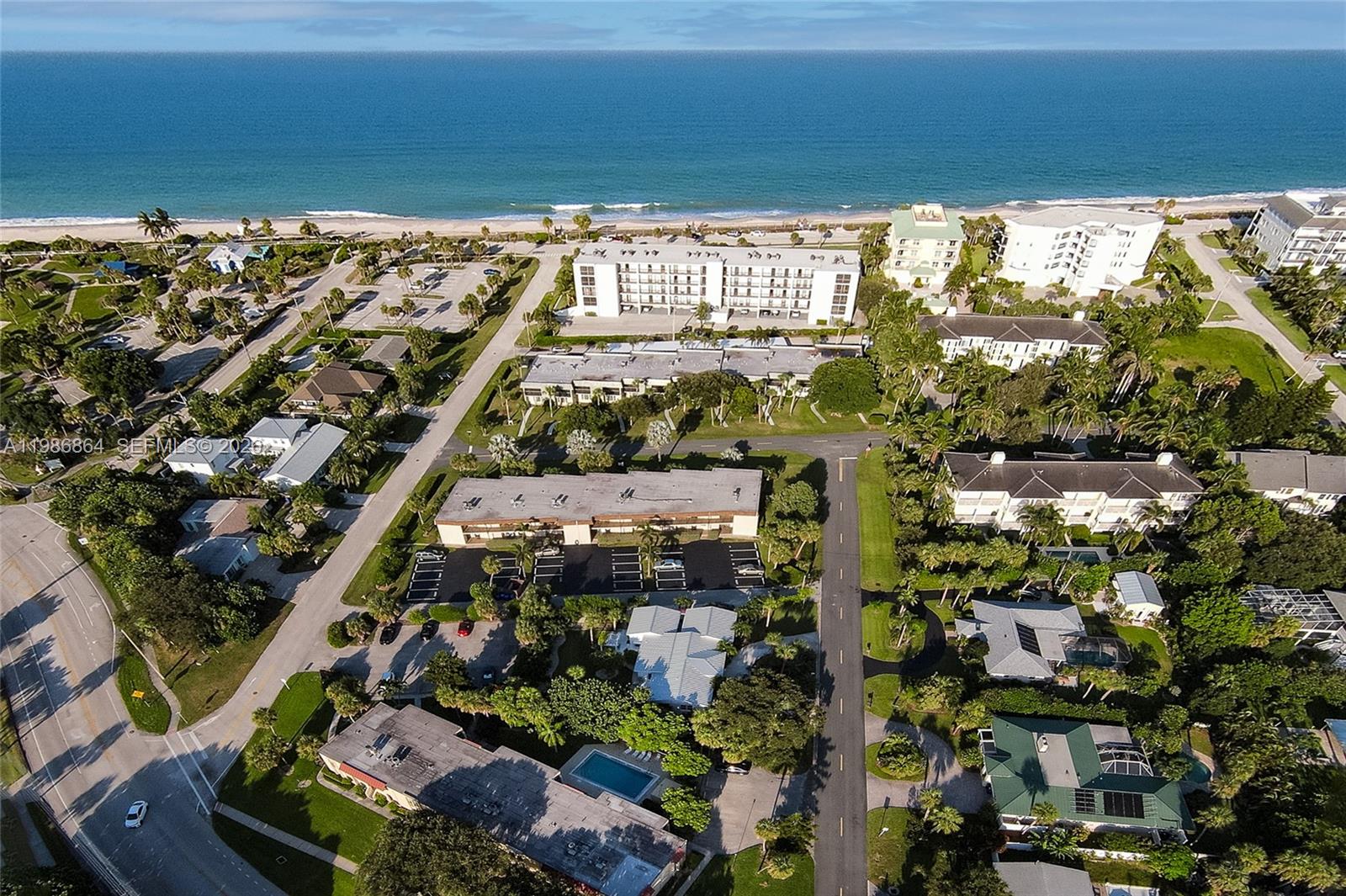An aerial view shows a coastal neighborhood with apartment buildings, parking lots, and palm trees — 4150 Highway A1A # 111, Vero Beach FL 32963, VERO BEACH, FL