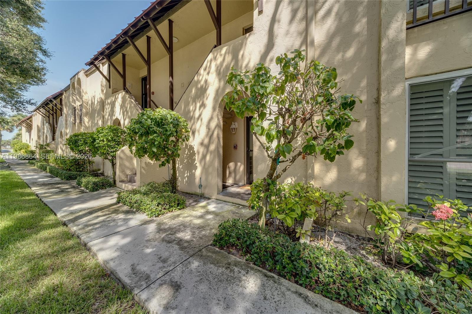 A tan stucco apartment building exterior features arched entryways and a concrete walkway — 4150 Highway A1A # 111, Vero Beach FL 32963, VERO BEACH, FL