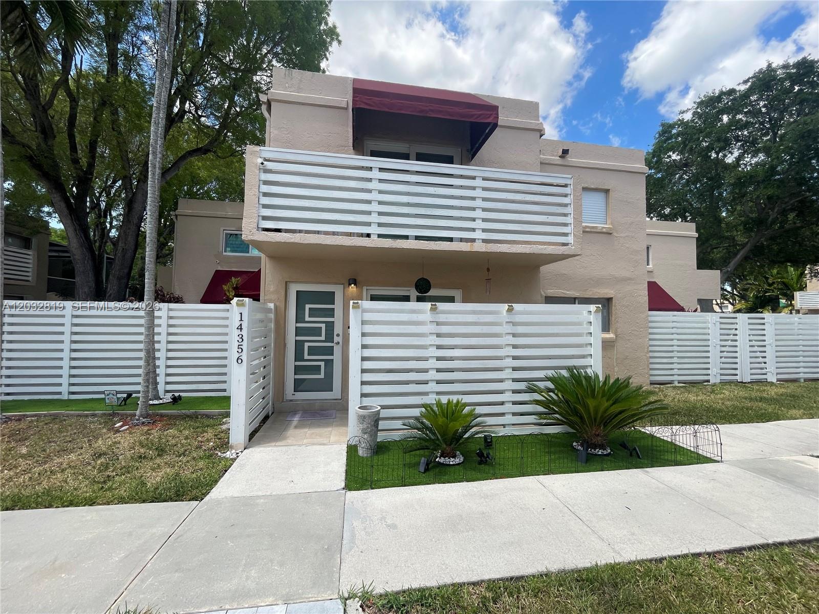 A two-story tan house features a white horizontal slat fence and a second-floor balcony — 14356 SW 96th Ter, Miami FL 33186, MIAMI, FL