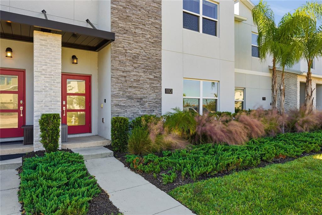 The exterior of a modern townhouse features a red front door and stone facade accents — 1112 CHALLENGE DRIVE, DAVENPORT, FL
