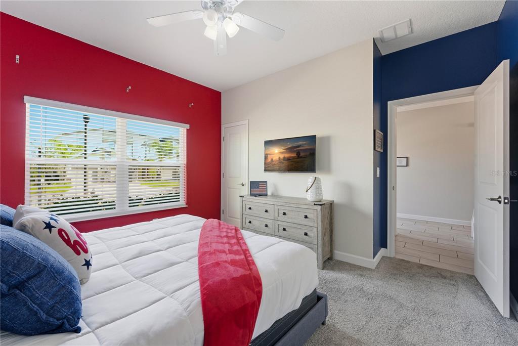 A bedroom features a red accent wall, a white bed, a dresser, and a ceiling fan — 1112 CHALLENGE DRIVE, DAVENPORT, FL