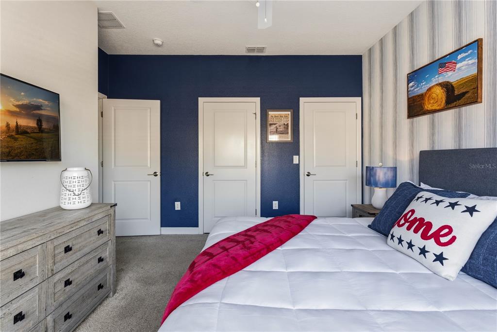 A bedroom features a bed, a dresser, three white doors, and a dark blue wall — 1112 CHALLENGE DRIVE, DAVENPORT, FL