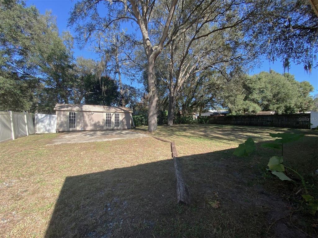 A backyard features a shed, a concrete patio, large trees, and a wooden fence — 11585 SE 129TH LANE, OCKLAWAHA, FL