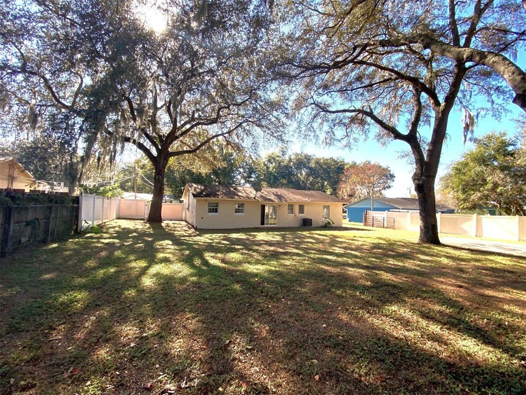 A backyard view of a single-story house with large oak trees and a white fence — 11585 SE 129TH LANE, OCKLAWAHA, FL