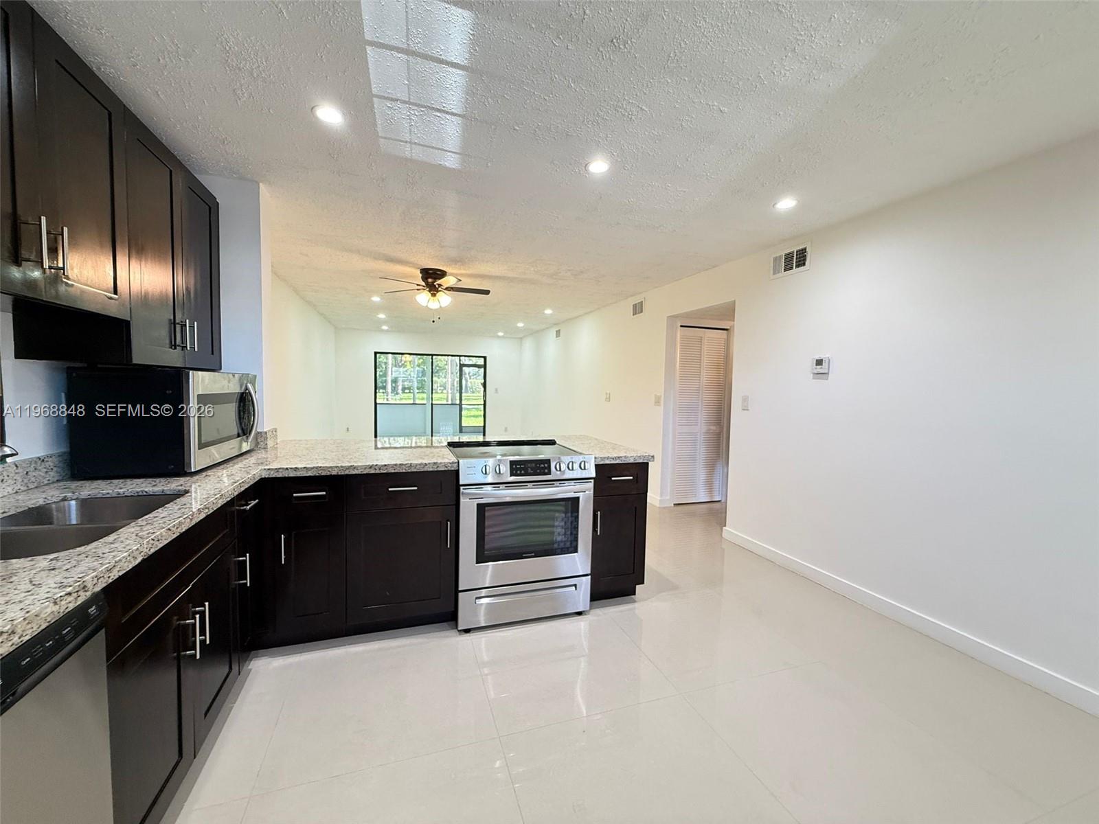 A kitchen with dark cabinets, granite countertops, and stainless steel appliances opens to a living area — 6095 N Sabal Palm Blvd # 103, Tamarac FL 33319, TAMARAC, FL